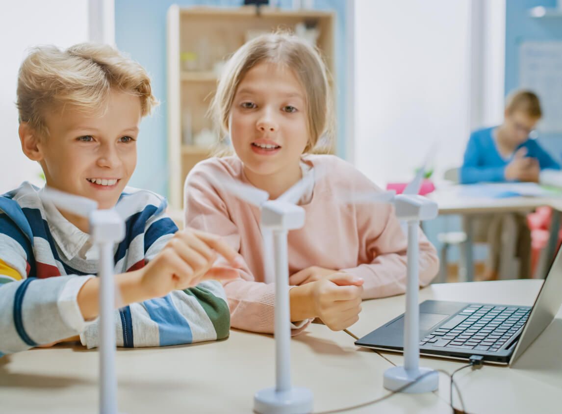 Dwoje uczniów obserwuje modele turbin wiatrowych podłączone do laptopa