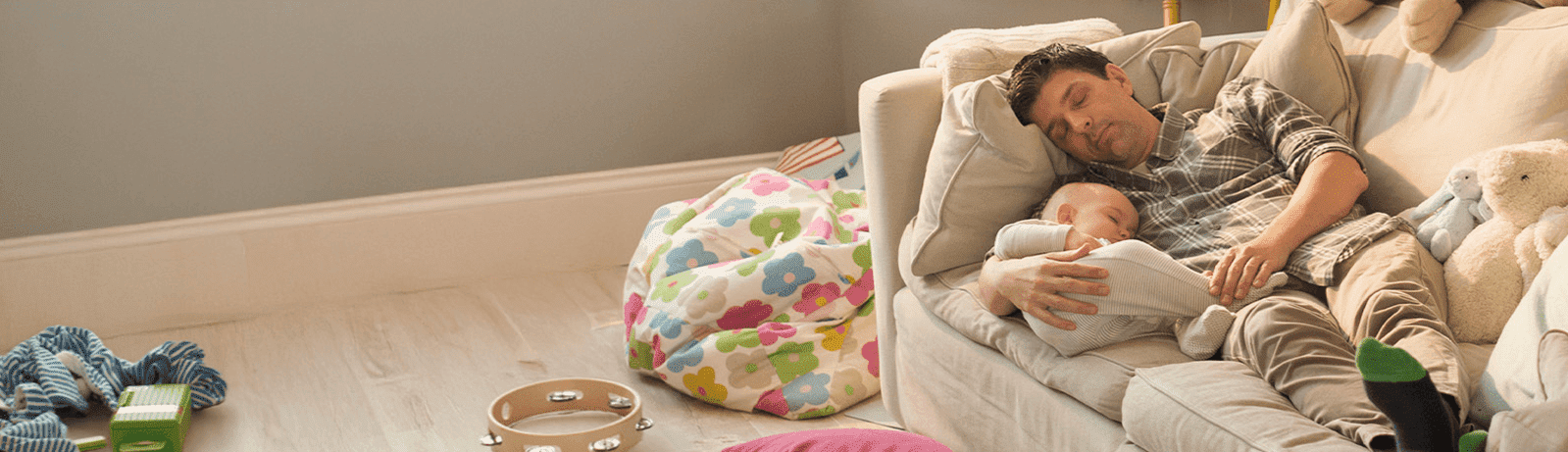 Mężczyzna odpoczywa na kanapie, trzymając śpiące dziecko na rękach — spokojna, domowa scena symbolizująca bezpieczeństwo i spokój w domu.