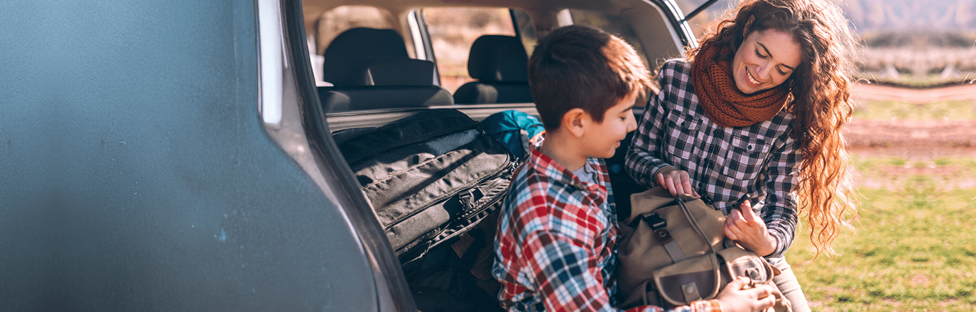 Kobieta i chłopiec pakują torbę do bagażnika samochodu w słoneczny dzień