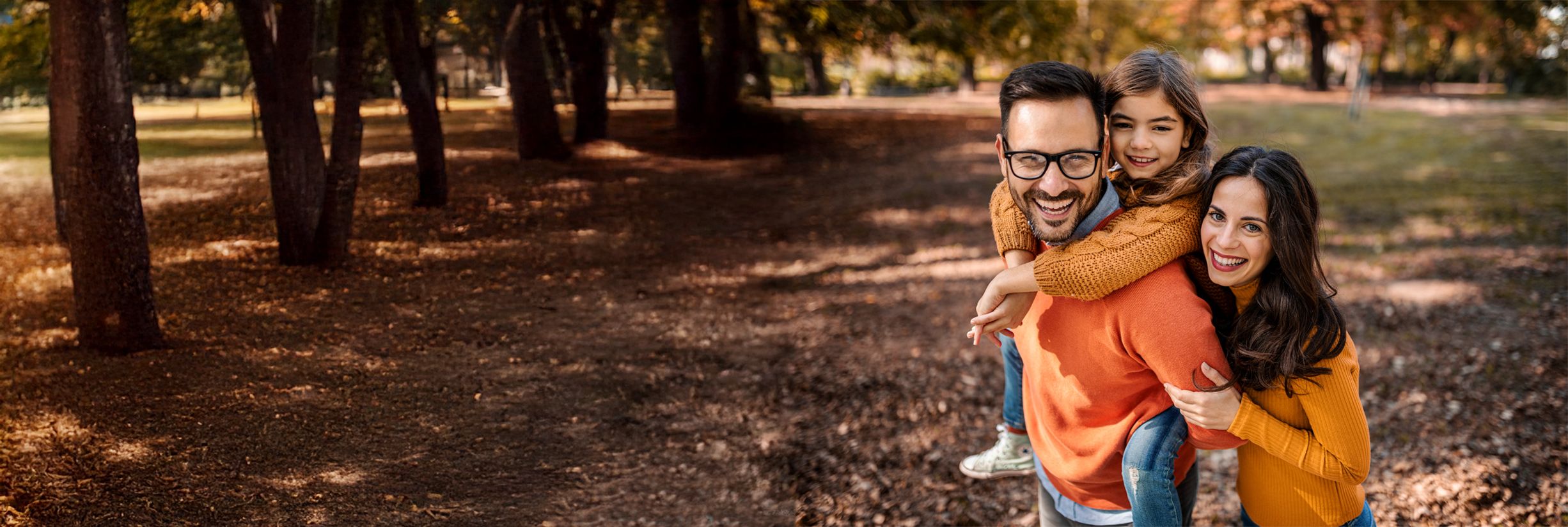 Uśmiechnięta rodzina – ojciec, matka i córka – spędzają razem czas w parku jesienią, ciesząc się wspólną zabawą i bliskością.