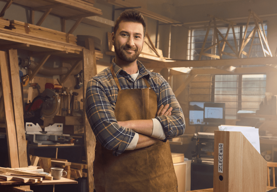 Dwie osoby, kobiety, siedzą przy stole w salonie kosmetycznym. Kobieta siedząca przodem uśmiecha się.